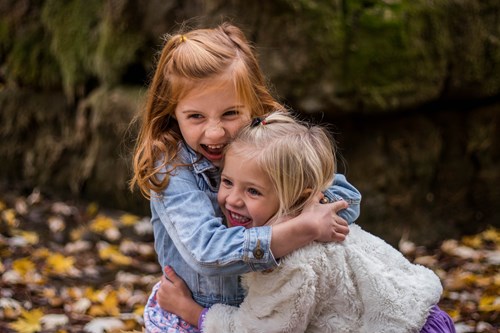 two girls hugging and laughing outside in the leaves in Farmington Hills MI